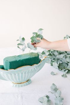 a hand reaching for a piece of cake in a bowl with greenery on the table