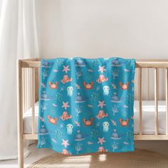 a baby crib with a blue and pink mermaid themed blanket hanging from it's side