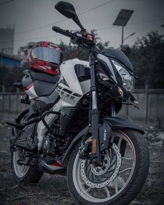 a white and black motorcycle parked on top of a dirt field next to a fence