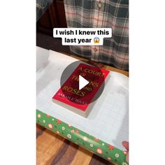 a person holding a book on top of a wooden table next to a green box