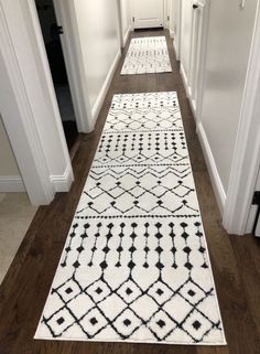 a long hallway with white and black rugs on the floor next to an open door