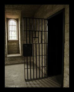 an empty jail cell with bars on the door and windows in the wall behind it