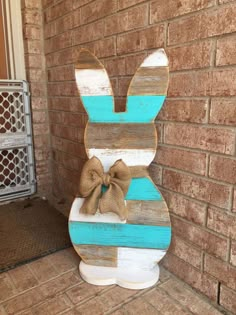 a wooden bunny with a bow on it's head sitting in front of a brick wall