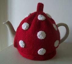 a knitted tea cosy with white polka dots on the top and bottom, sitting on a table