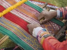 two people are weaving on a colorful blanket