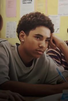 a young man sitting in front of a desk with papers on the wall behind him