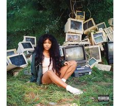 a woman sitting on the ground surrounded by old tvs and television sets in grass