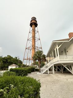 a tall tower sitting next to a lush green forest filled with trees and bushes on top of a sandy beach