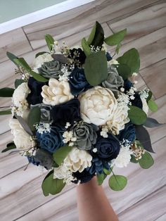 a bridal bouquet with blue, white and grey flowers on it is held by someone's hand