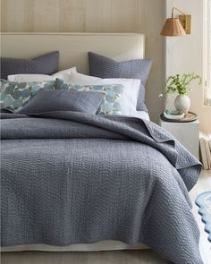 a bed with blue comforter and pillows in a bedroom next to a lamp on the wall