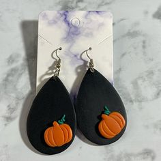 a pair of black and orange earrings with pumpkins on them sitting on a marble surface