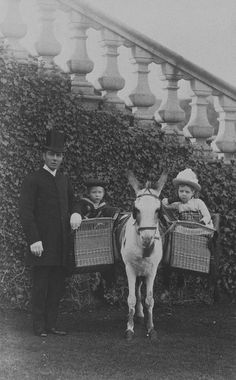 an old black and white photo shows two children standing next to a donkey with baskets on its back