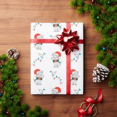 a christmas present wrapped in white paper with red ribbon and reindeers on it next to pine branches