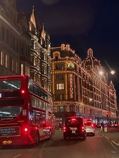 two double decker buses driving down the street in front of buildings with christmas lights on them