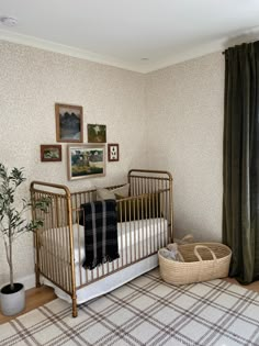 a baby crib in the corner of a room with pictures on the wall and a potted plant next to it