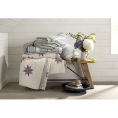 a pile of towels sitting on top of a wooden table next to a vase with flowers