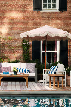 a couch and table sitting next to a swimming pool with an umbrella over it's head