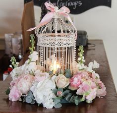 a birdcage filled with flowers and candles on top of a wooden table next to a chalkboard