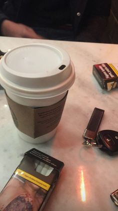 a cup of coffee sitting on top of a table next to some cell phones and keys