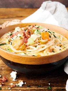 a wooden bowl filled with pasta and vegetables on top of a table next to bread