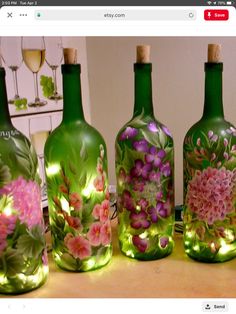 three green glass bottles with flowers painted on them and wine glasses in the back ground