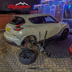 two cars are parked in front of a house with christmas lights on the roof and one is upside down