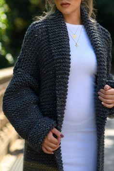 a woman is wearing a black crochet cardigan and white top while standing on a bridge