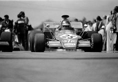 a man driving a race car down a track with other people watching from the sidelines