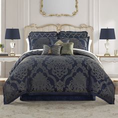 a bed with blue comforter and pillows in a room next to two lamps on either side of the bed