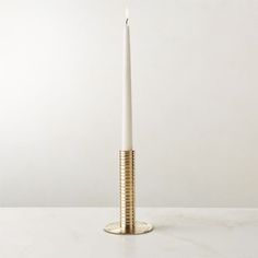 a white candle sitting on top of a table next to a metal holder with a gold stripe