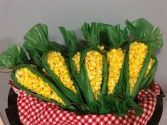 corn on the cob with green leaves and red checkered table cloth in front of grey wall