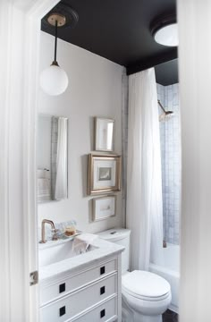 a white bathroom with black ceiling and gold accents on the walls, along with two framed pictures