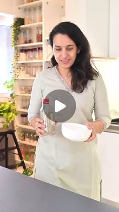 a woman standing in front of a kitchen counter holding a jar and spoon with food on it