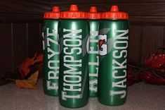 three green and orange sports bottles sitting next to each other on a counter with autumn leaves