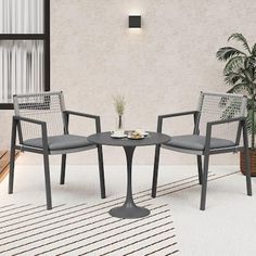 two chairs and a table in front of a wall with a potted plant on it