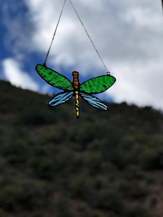 a stained glass dragon hanging from a chain in front of a cloudy blue sky with white clouds