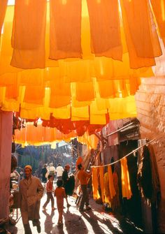 people are walking through an alley with yellow cloths hanging from the ceiling over them