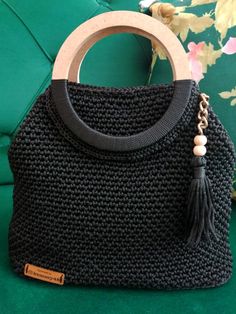 a black handbag with a wooden handle and tassel hanging from it's side