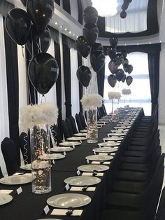 a long table is set up with black and white balloons, silverware, and place settings