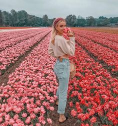 a woman standing in the middle of a field with pink tulips behind her