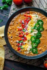 a black bowl filled with beans, cheese and peppers next to tortilla chips