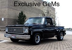 an old black pickup truck parked in front of a brick building with the words executive gems on it