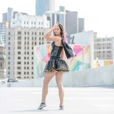 a woman in a short black dress is standing on the roof with her hands behind her head