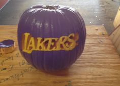 a purple pumpkin with the word lakers painted on it sitting on a wooden table next to a piece of wood