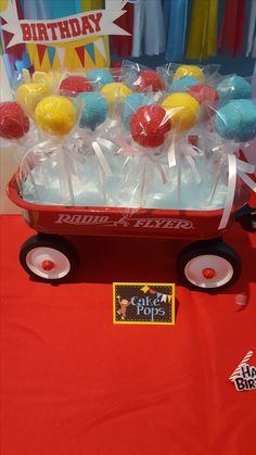 a wagon filled with lollipops on top of a red cloth covered table