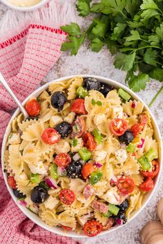 a white bowl filled with pasta salad next to parsley and garlic on a red checkered towel