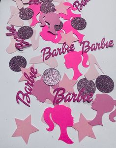 some pink and purple cut outs on a white table with glitter confetti in the shape of barbie