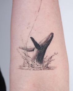 a tattoo on the arm of a woman with a whale tail coming out of water