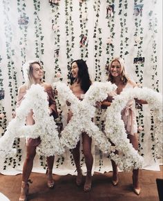 three beautiful women standing next to each other in front of a wall covered with flowers