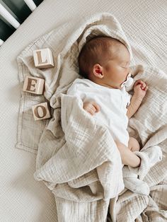 a baby wrapped in a blanket laying on top of a bed next to blocks that spell out the word love